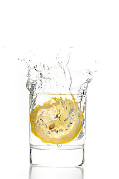 一片新鲜的柠檬片掉入玻璃水杯中的瞬间,水花飞溅空中