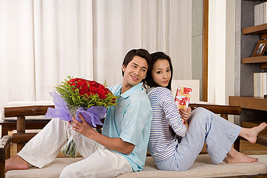 一对年轻的夫妻抱着鲜花背靠背坐在一起