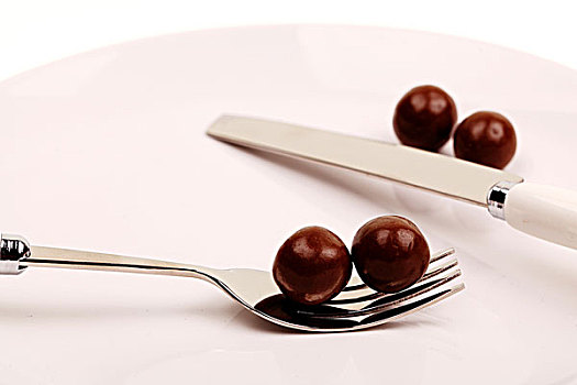 白色盘子中的四个圆形棕色巧克力豆和银色刀叉