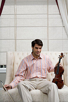 一位先生拿着小提琴坐在沙发上