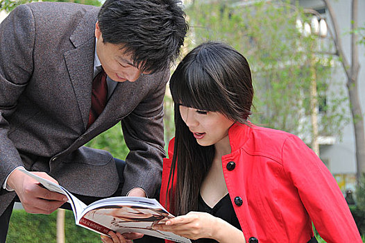 一对年轻人在公园内一起看杂志