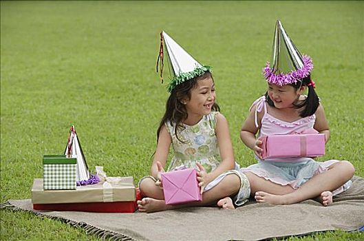 两个女孩,戴着,派对帽,坐,野餐毯,拿着,粉色,礼盒