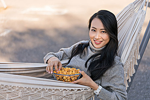 年轻女子坐在吊床上吃爆米花