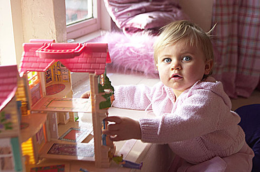 女孩,看镜头,玩具屋,人,孩子,幼儿,1-2岁,金发,蓝眼睛,衣服,粉色,照料,玩具,房子,室内,在家