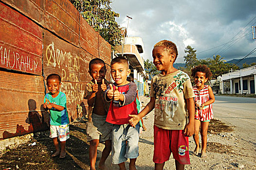group,of,timorese,children,with,thumbs,up,in,the,street,under,dark,clouds