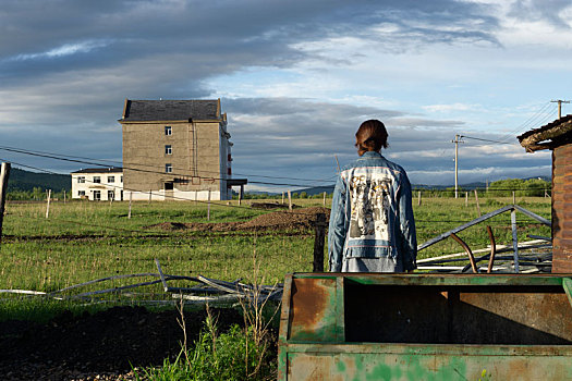 生锈的铁箱旁一个女孩背向画面遥望草原
