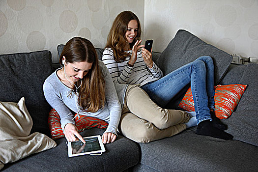 两个,女孩,坐,沙发,一个,听,耳机,音乐,平板电脑,玩,苹果手机,智能手机