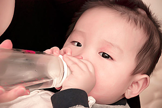 躺在母亲怀里喝水的一名7个月大的男婴