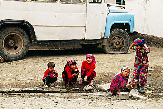 tajikistan,penjakent,children,in,traditional,dress,doing,the,dishes,with,old,schoolbus,background