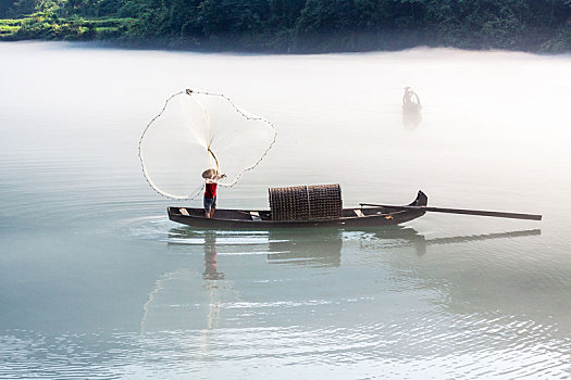 渔夫在飘渺晨雾的湖泊中打鱼