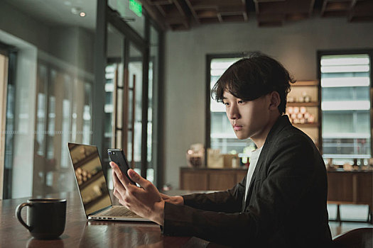一名亚洲男子在咖啡馆手持智能电话