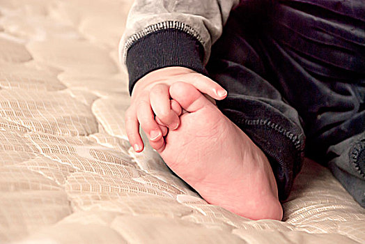 一名7个月大的男婴的小手抓着自己的小脚