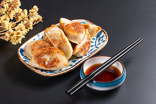 色泽金黄的煎饺子盛放在青花盘子中摆放在黑色背景上