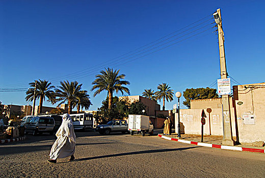 algeria,ben,isguen,rear,view,of,a,person,walking,on,street,by,sign,board