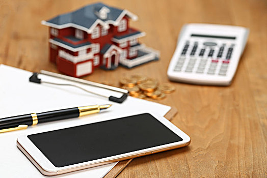 房屋模型,手机,钢笔和硬币放在桌面上