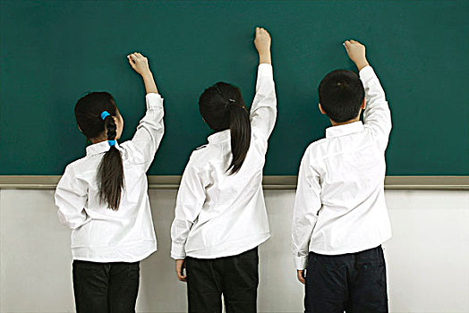 教室里面朝黑板站着手握粉笔在画画的三个小学生