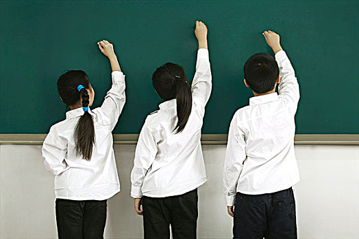教室里面朝黑板站著手握粉筆在畫畫的三個小學生