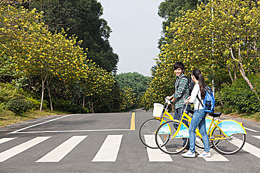 年轻大学生情侣在校园里骑车过马路