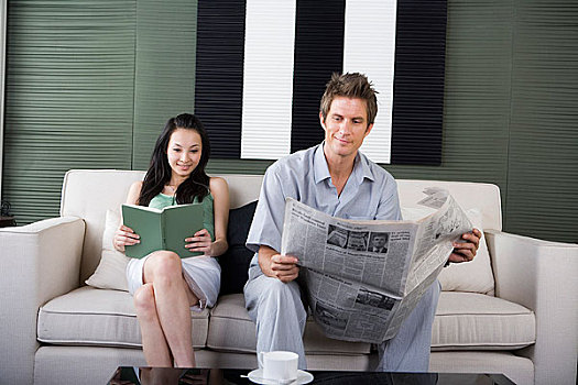 一对年轻夫妻坐在沙发上看书和报