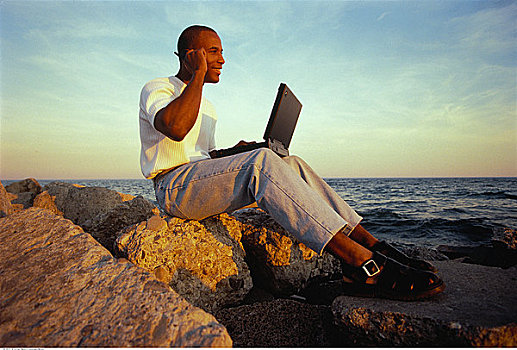 男人,坐,岩石上,靠近,水,手机,笔记本电脑