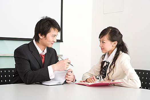 一位女职员和一位男职员坐在会议桌前讨论工作内容