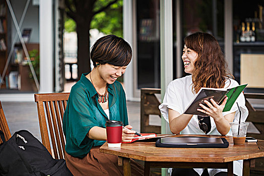 两个女人,黑发,穿,绿色,白衬衫,坐,桌子,街头咖啡馆,拿着,数码,微笑