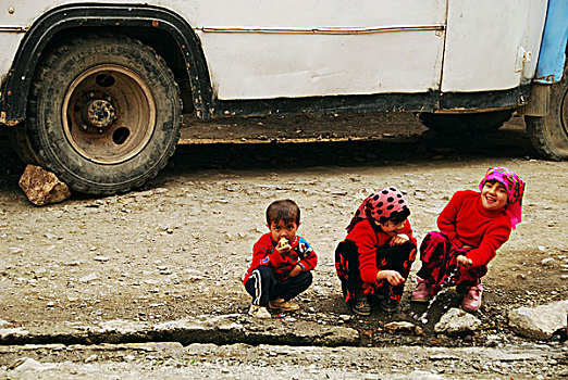 tajikistan,penjakent,children,in,traditional,dress,doing,the,dishes,with,old,schoolbus,background