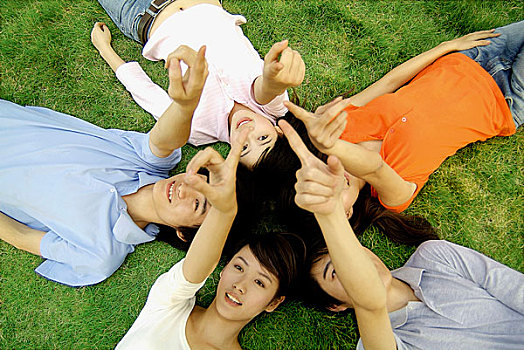 草地上躺着形成圆形用手指着上空的五个年轻男女特写