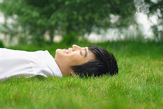 闭着眼睛面带微笑躺在草地上的年轻男人