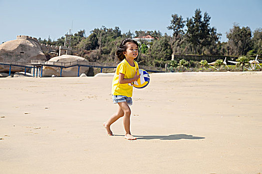 小女孩抱着排球在沙滩上奔跑