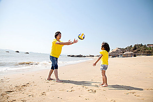 年轻父亲和女儿在沙滩上玩排球