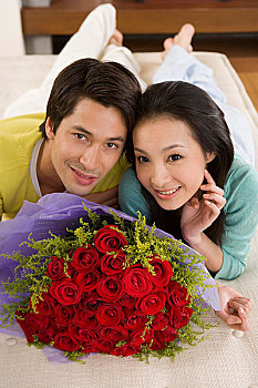 一对年轻的夫妻趴在床上看着面前摆放的鲜花