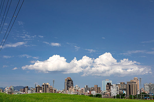 堤防公园绿草岥上的电塔,蓝天白云下的城市