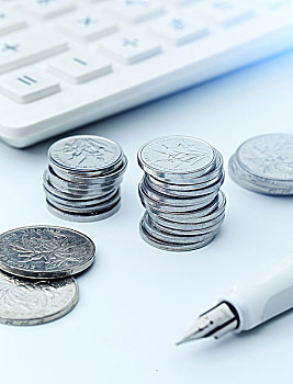 计算器硬币和钢笔放在白色桌面上