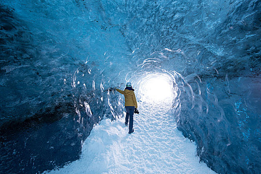 一名穿着黄色衣服的女性站在冰岛蓝冰洞中
