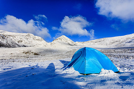 晴天雪山脚下的蓝色帐篷