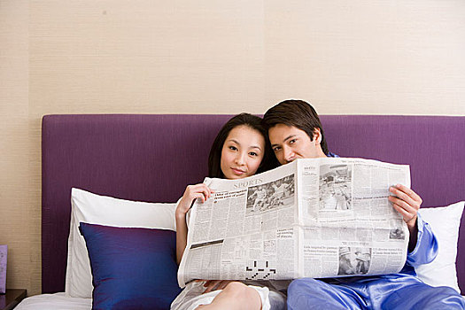 一对年轻的夫妻坐在床上一起看报纸