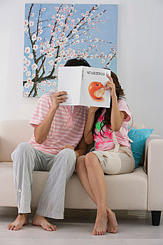 一对年轻的夫妇拿着书挡住脸坐在沙发上