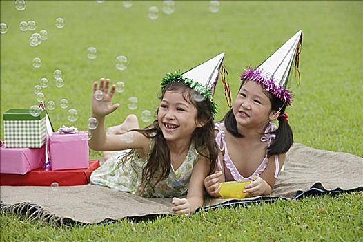 两个女孩,戴着,派对帽,躺着,野餐毯,看,泡泡