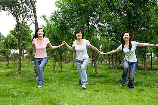 草地上手牵手奔跑的三个女孩