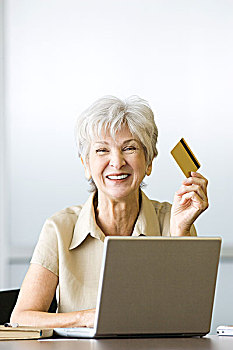 老年,女人,坐,书桌,拿着,信用卡,使用笔记本,看镜头,微笑