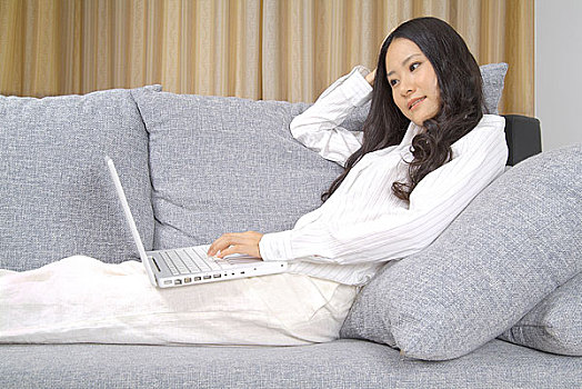 躺在沙发上一手抱头使用电脑的年轻女人