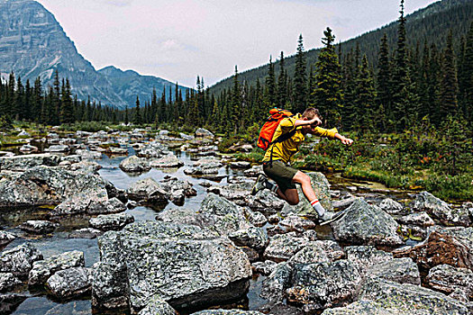 侧面视角,中年,男人,背包,跳跃,上方,岩石,河床,冰碛湖,班芙国家公园,艾伯塔省,加拿大