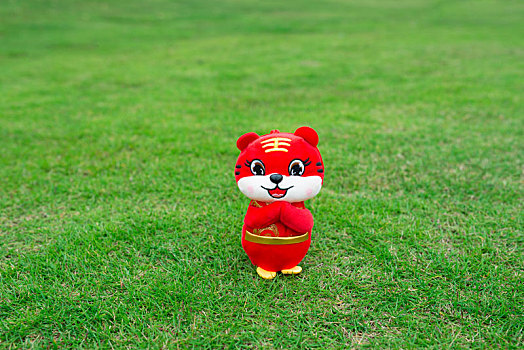 红色的可爱卡通老虎生肖玩偶站在绿色草坪上作揖拱手拜年