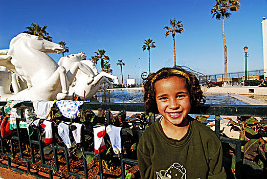 algeria,alger,portrait,of,a,smiling,girl,standing,in,front,railing,with,socks,drying,on,it,sculpture,horse,and,swimming,pool,background