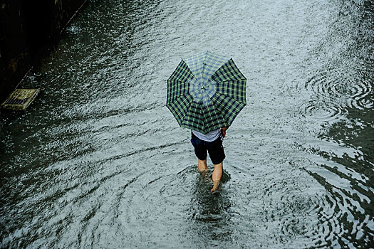 一个撑伞男子挽起裤脚在积水道路上涉水