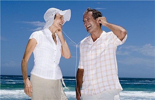 老年,夫妻,站立,海滩,听,mp3播放器,分享,耳机,微笑,侧面视角