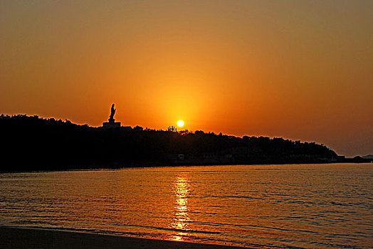 海边夕阳中的金身观音像剪影