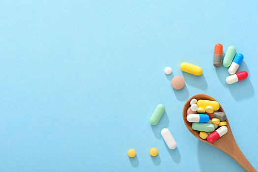 蓝色背景上的大量药物和装满药品的木勺,医疗健康概念