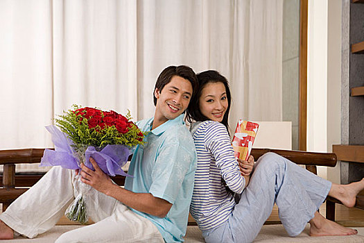 一对年轻的夫妻抱着鲜花背靠背坐在一起